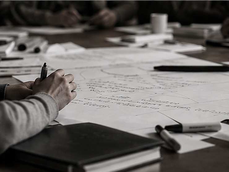 Hands writing on a large sheet of paper covered in notes and diagrams