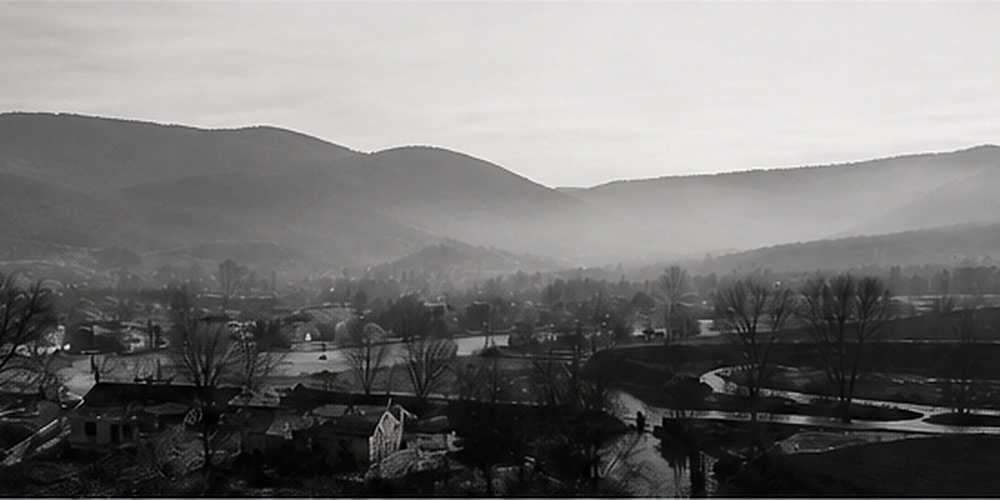 A valley town below wooded hills in flat winter light